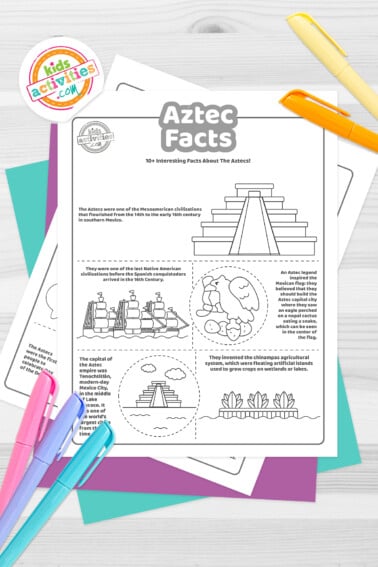 Black and white coloring pages with Aztec facts lying on top of blue-green and purple sheets with assorted crayons on a dark grey background.
