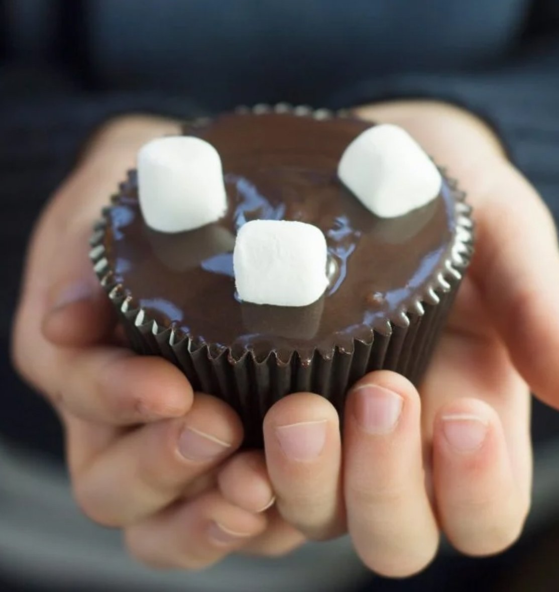 A kid holding a chocolate cupcake with marshmallows.
