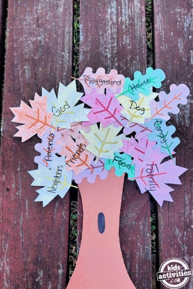 Paper Gratitude Tree- Leaves with colors, words, and brown construction paper trunk tree on distressed wood- Kids Activities Blog
