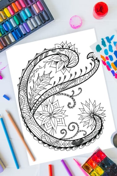 Zentangle alphabet coloring pages - letter e zentangle design on background of paint, colored pencils and art supplies