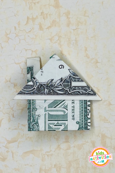 Finished result of a dollar bill origami home on top of a marble background