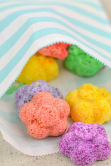 essential oils in a bath- fizzie flower bath bombs with purples, orange, yellow, and green bath bombs in a white and green paper bag- kids activities blog