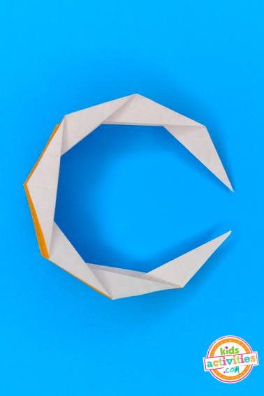 Final result of an origami moon made with yellow paper on top of a blue background. from Kids activities blog