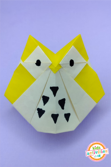 Final result of an origami owl made with yellow origami paper on top of a purple background.