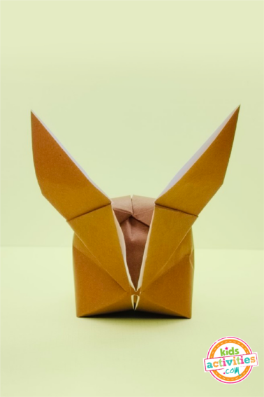 finished result of an origami rabbit made with brown origami paper on top of a green background.